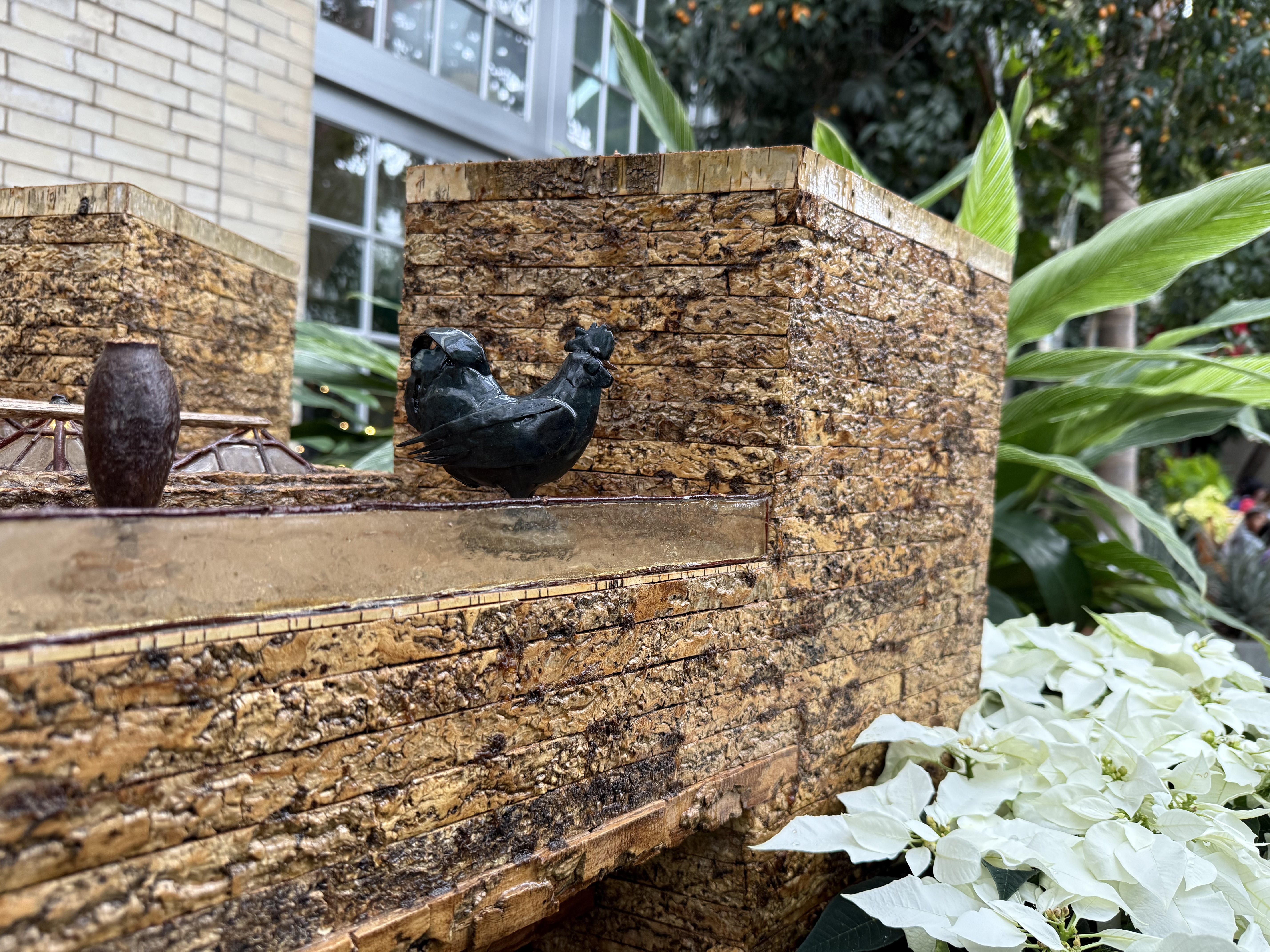 A 4" blue rooster model made from plant parts sit atop a model of the National Gallery of Art made from plant parts