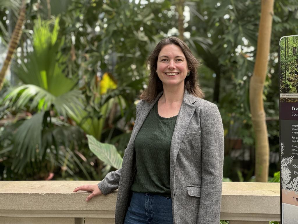 A woman stands in front of tropical plants in a Conservatory