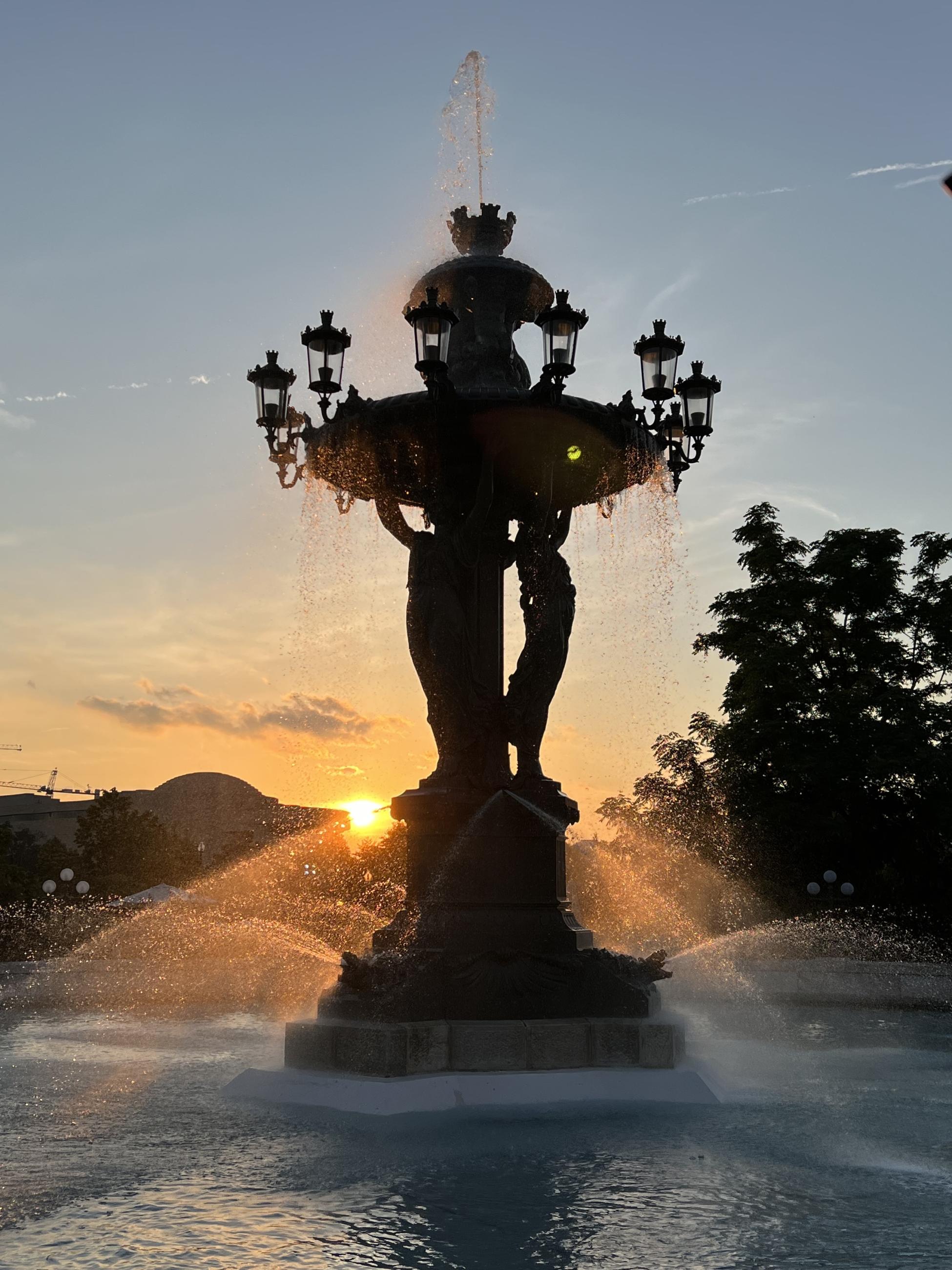 A 30 foot tall fountain sprays water with a golden sunset behind