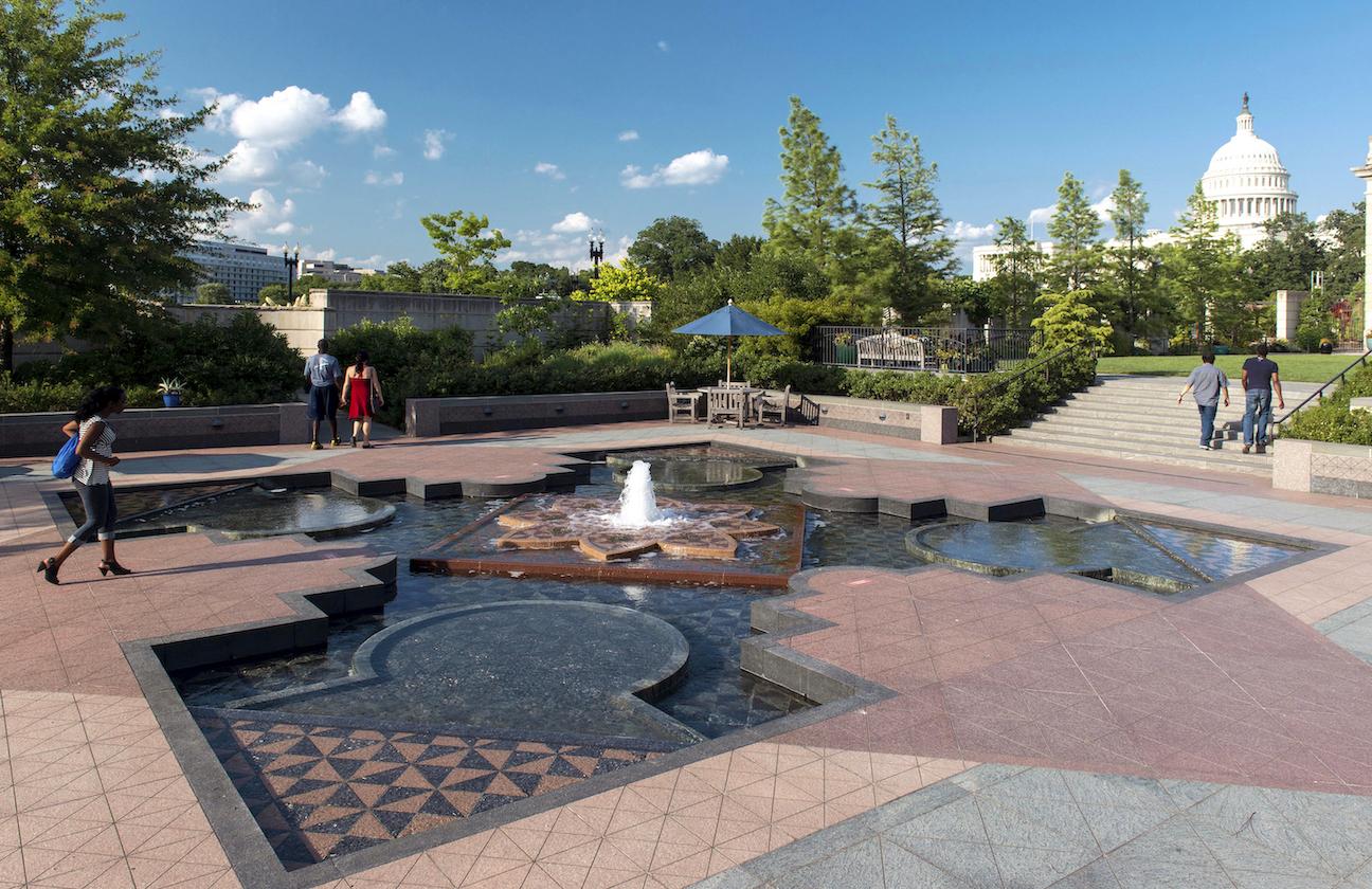 A large fountain with tile is surrounded by plants