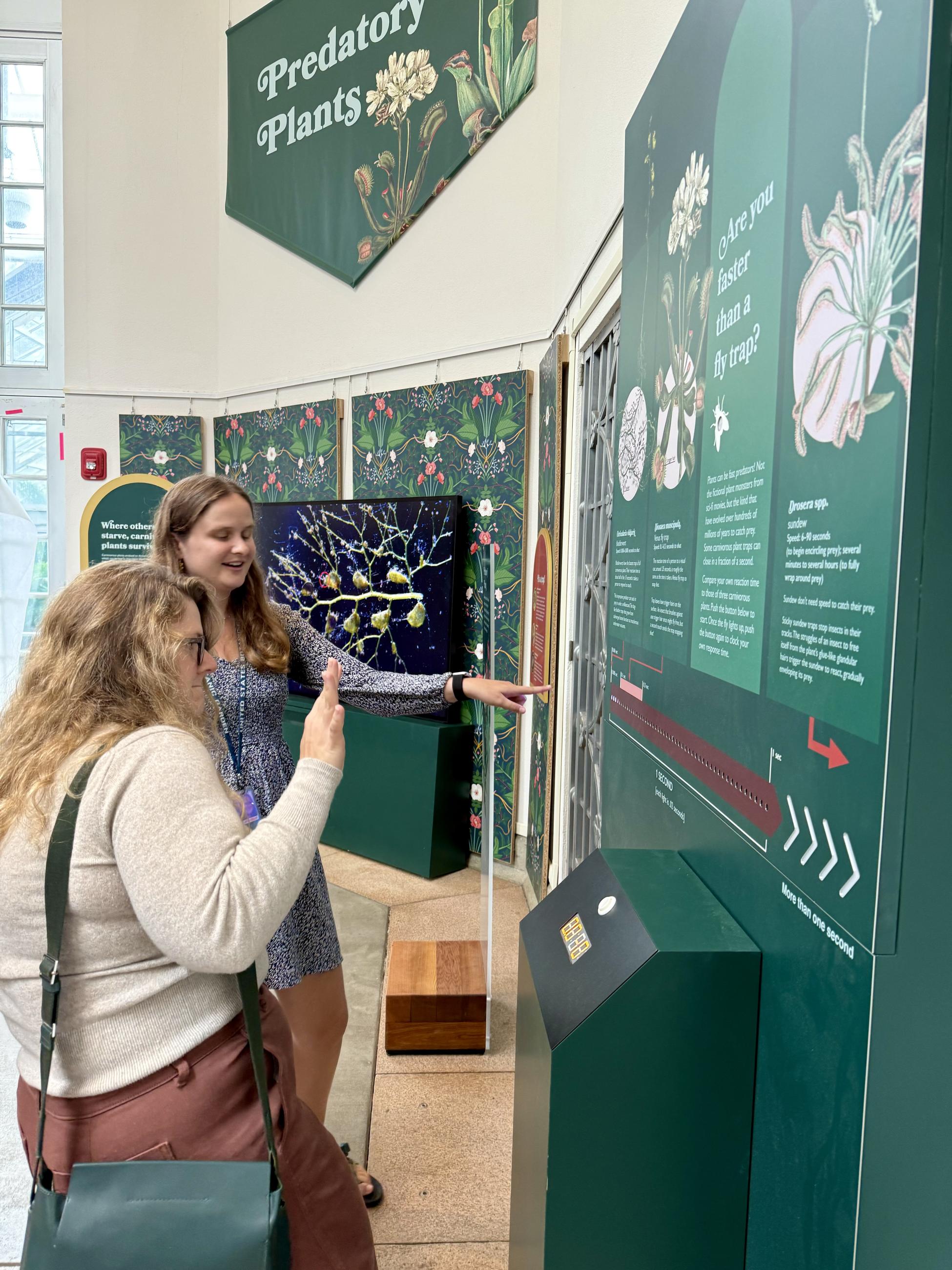 two young women tap a button to test the speed of their reaction against the speed of carnivorous plants